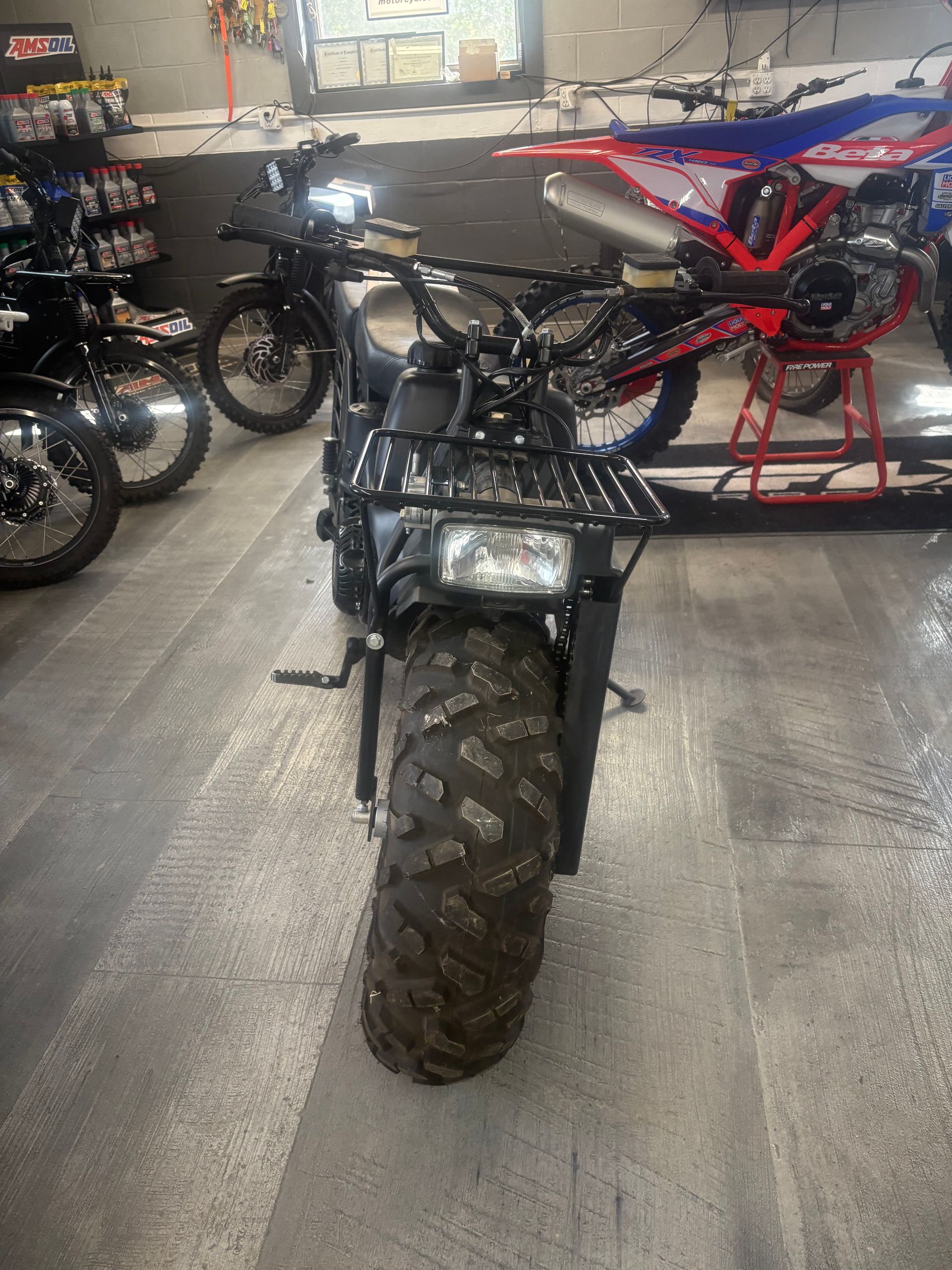 Black off-road motorcycle in a garage, facing forward with other dirt bikes in the background.