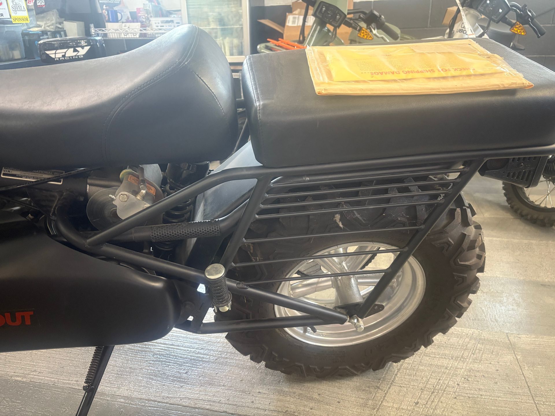 Black motorcycle seat and rear wheel with a yellow cargo bag in a garage.