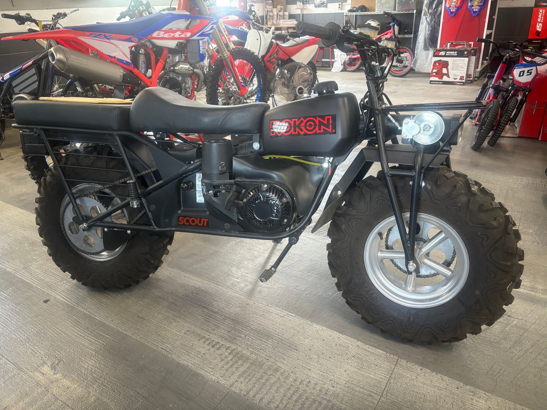 Black minibike with chunky tires and headlight displayed indoors in a motorcycle shop.