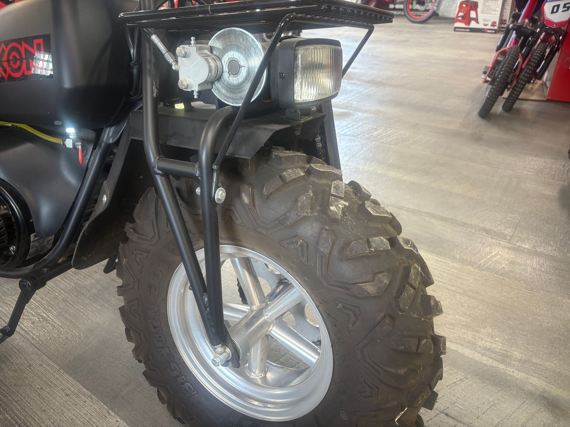 Close-up of a black off-road scooter’s front wheel and headlight inside a garage.