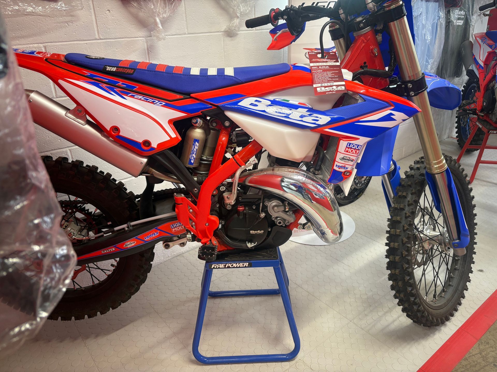 Red and blue dirt bike on a blue stand in a garage, side view