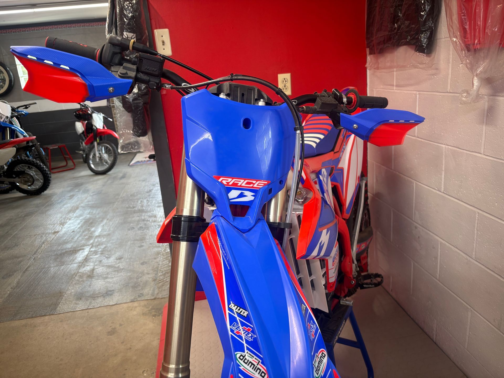 Blue and red motocross bike in a garage, viewed from the front.