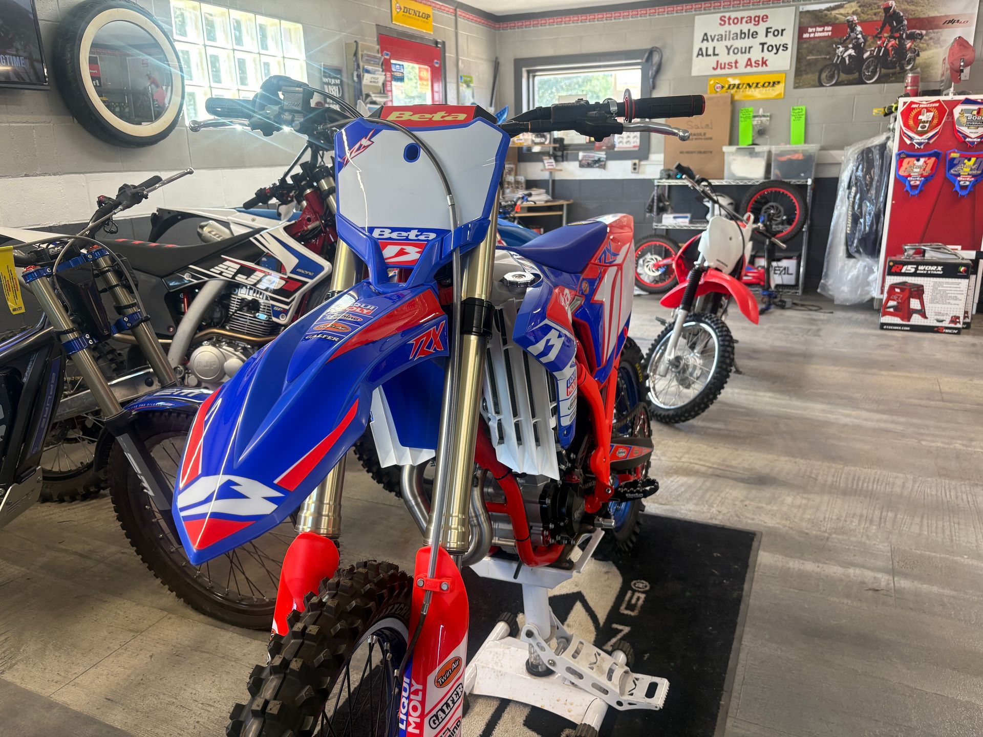 Blue and red dirt bike displayed in a motorcycle shop with other bikes in the background