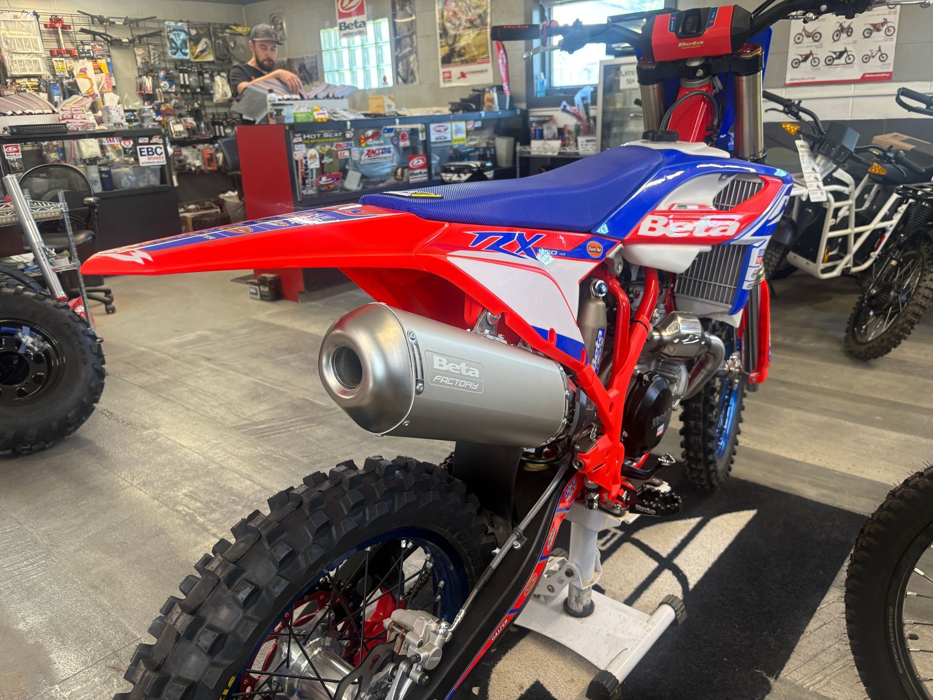 Red and blue dirt bike on display in a garage with a large silver exhaust pipe