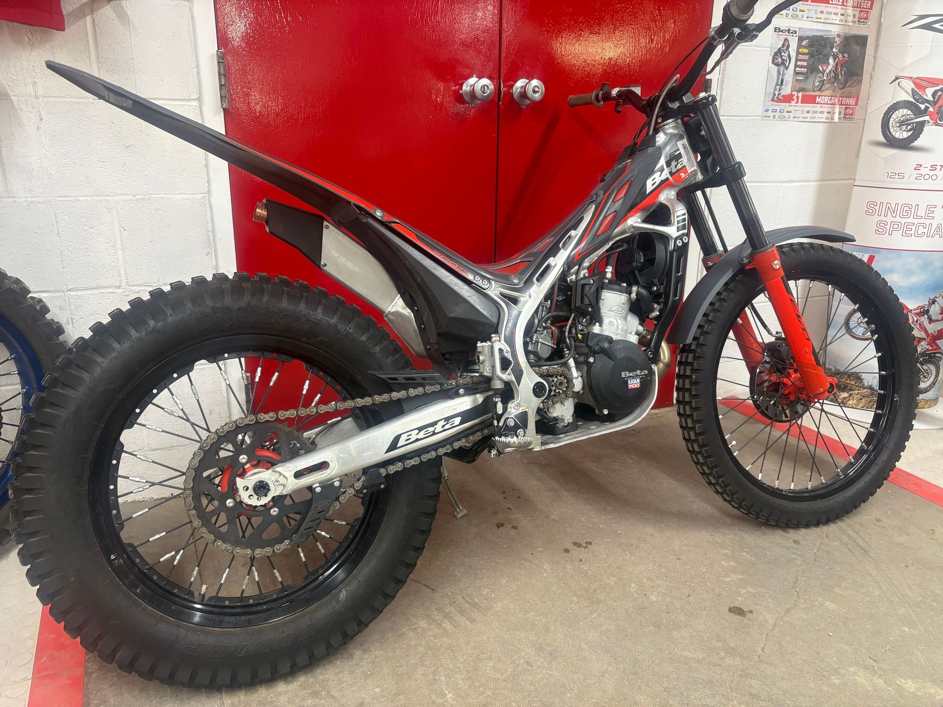 Black off-road motorcycle with knobby tires parked in a garage against red cabinets.