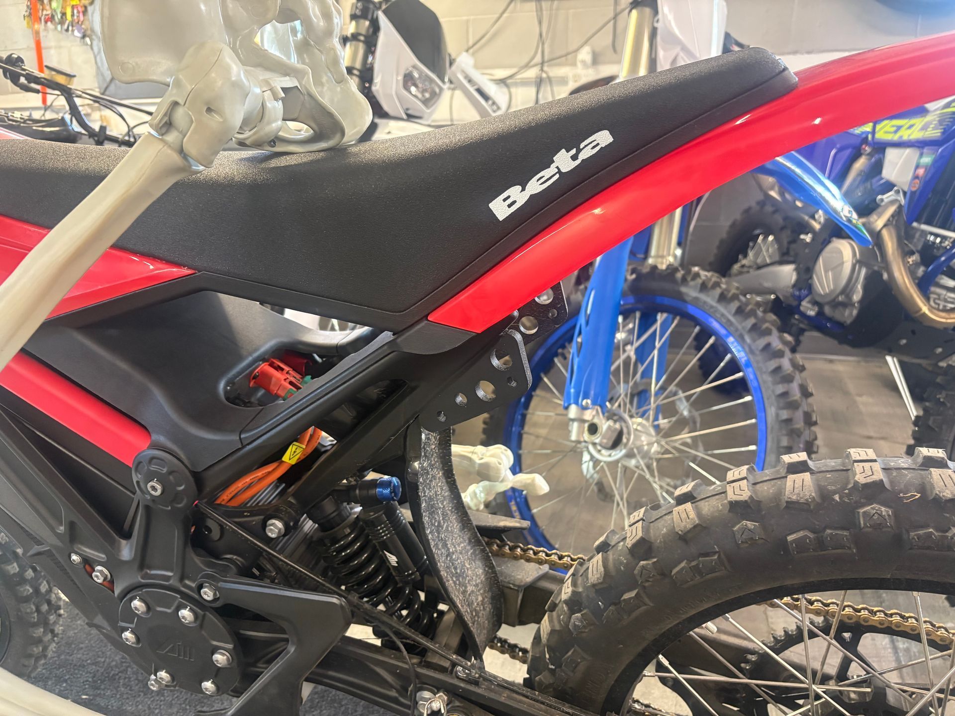 Red and black dirt bike with knobby tires, shown in a garage beside another motorcycle.