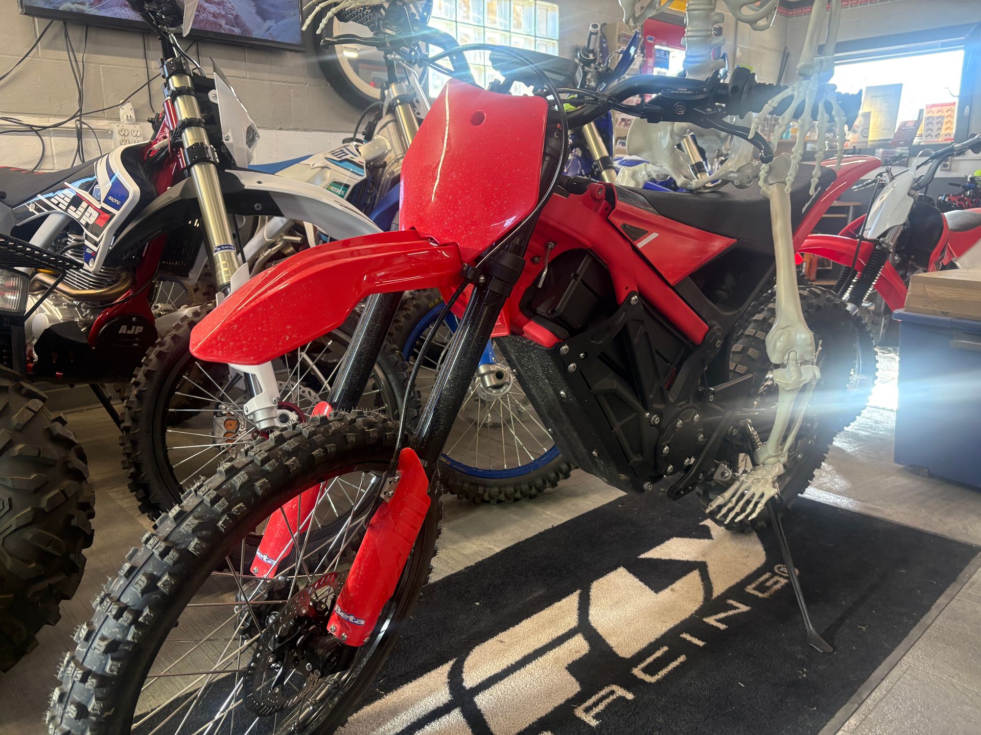Red dirt bike with black frame and knobby tires displayed in a showroom among other motorcycles.