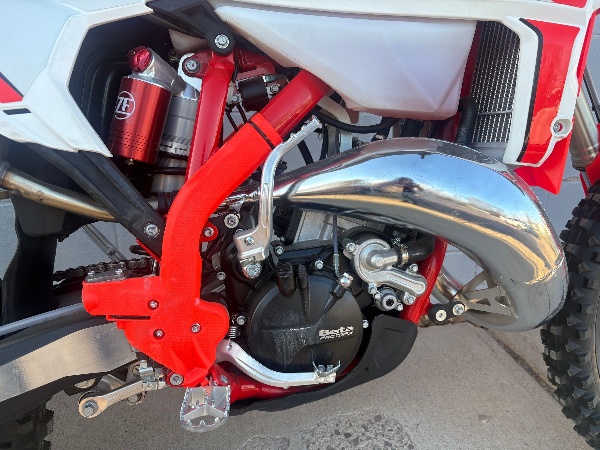 Close-up of a dirt bike engine and exhaust with a red frame and white body panel.