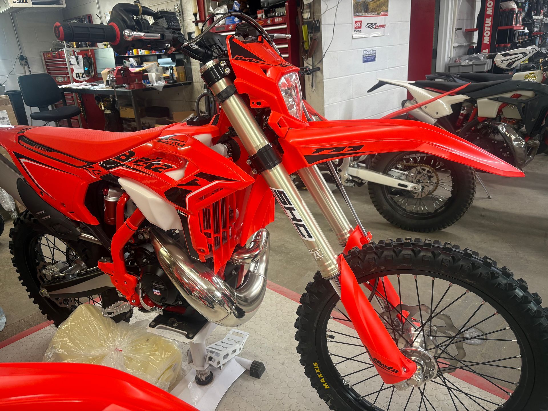 Red dirt bike in a workshop, shown from the front-left with bright red bodywork and knobby tires.