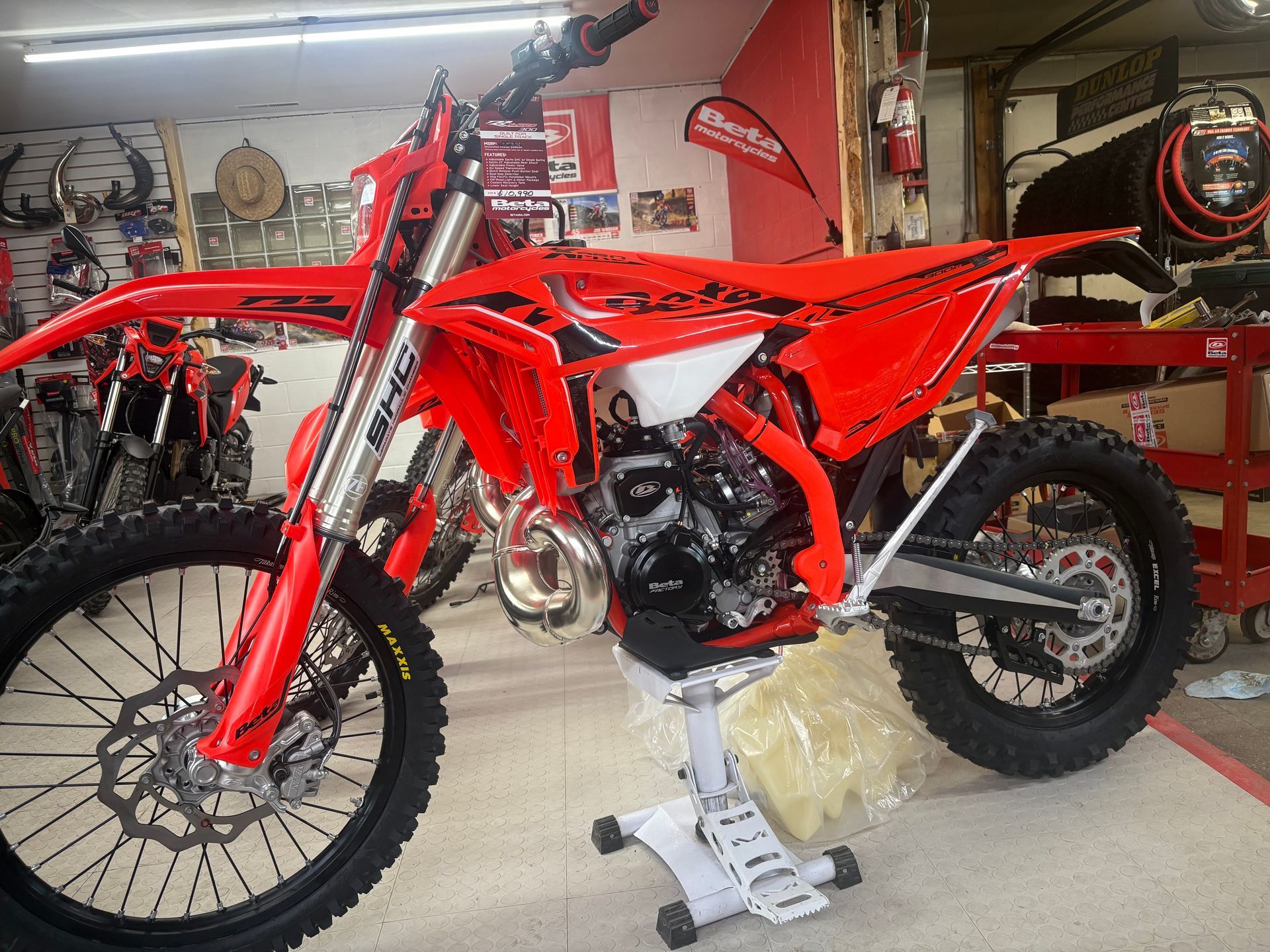 Red dirt bike on a stand in a workshop, with a second bike and tools in the background