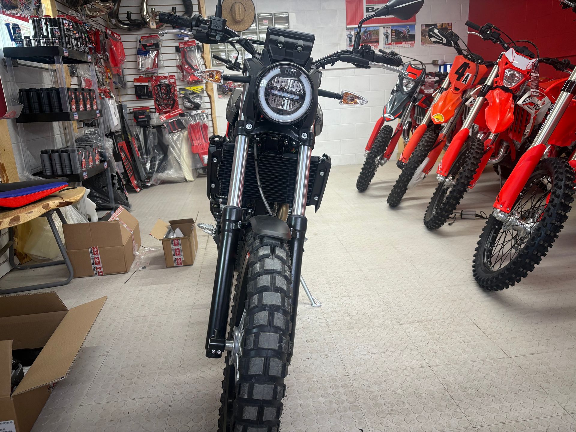 Black motorcycle centered in a shop aisle, with rows of red dirt bikes and parts in the background