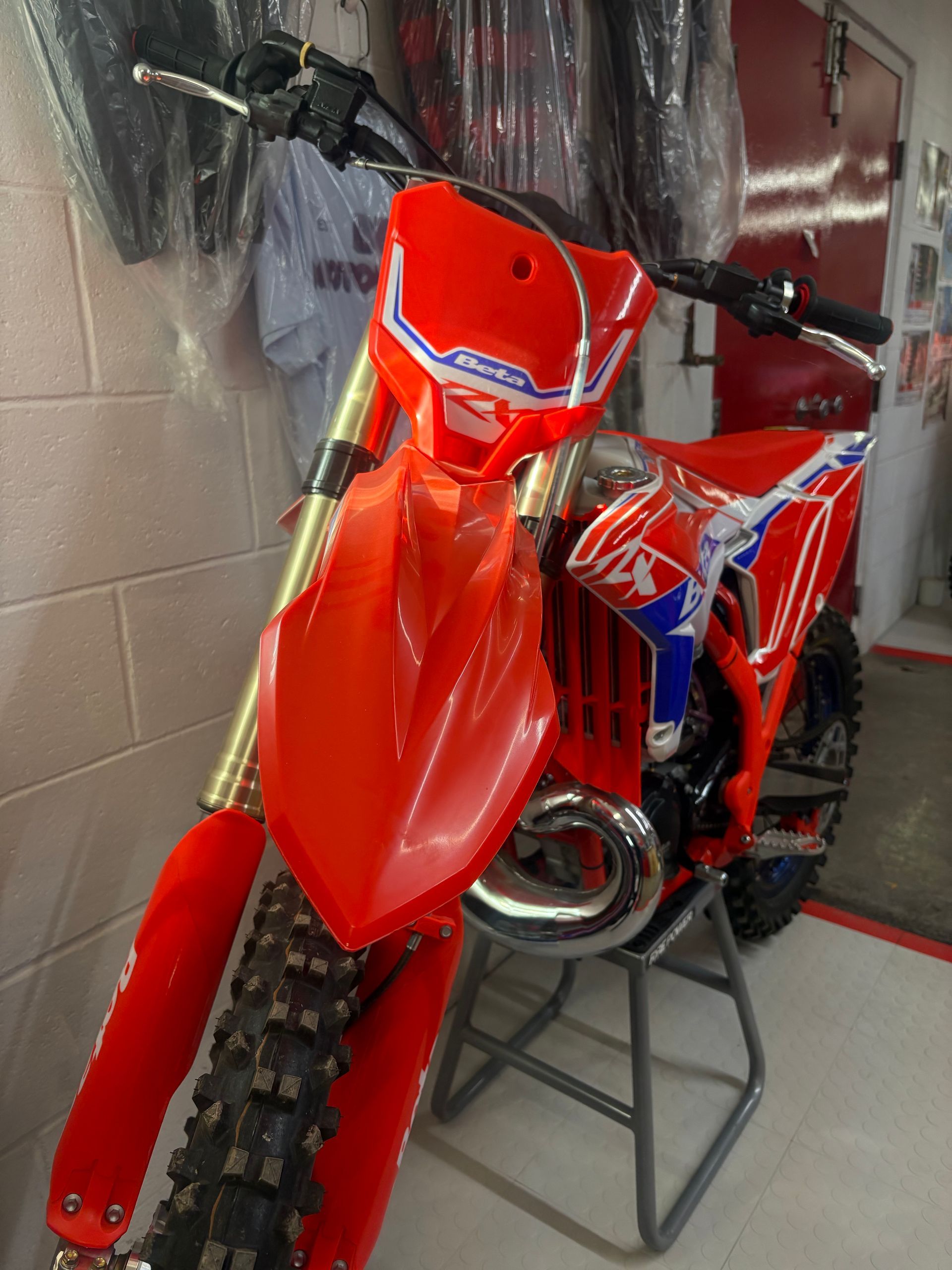 Red dirt bike with blue accents on a stand in a garage-like space