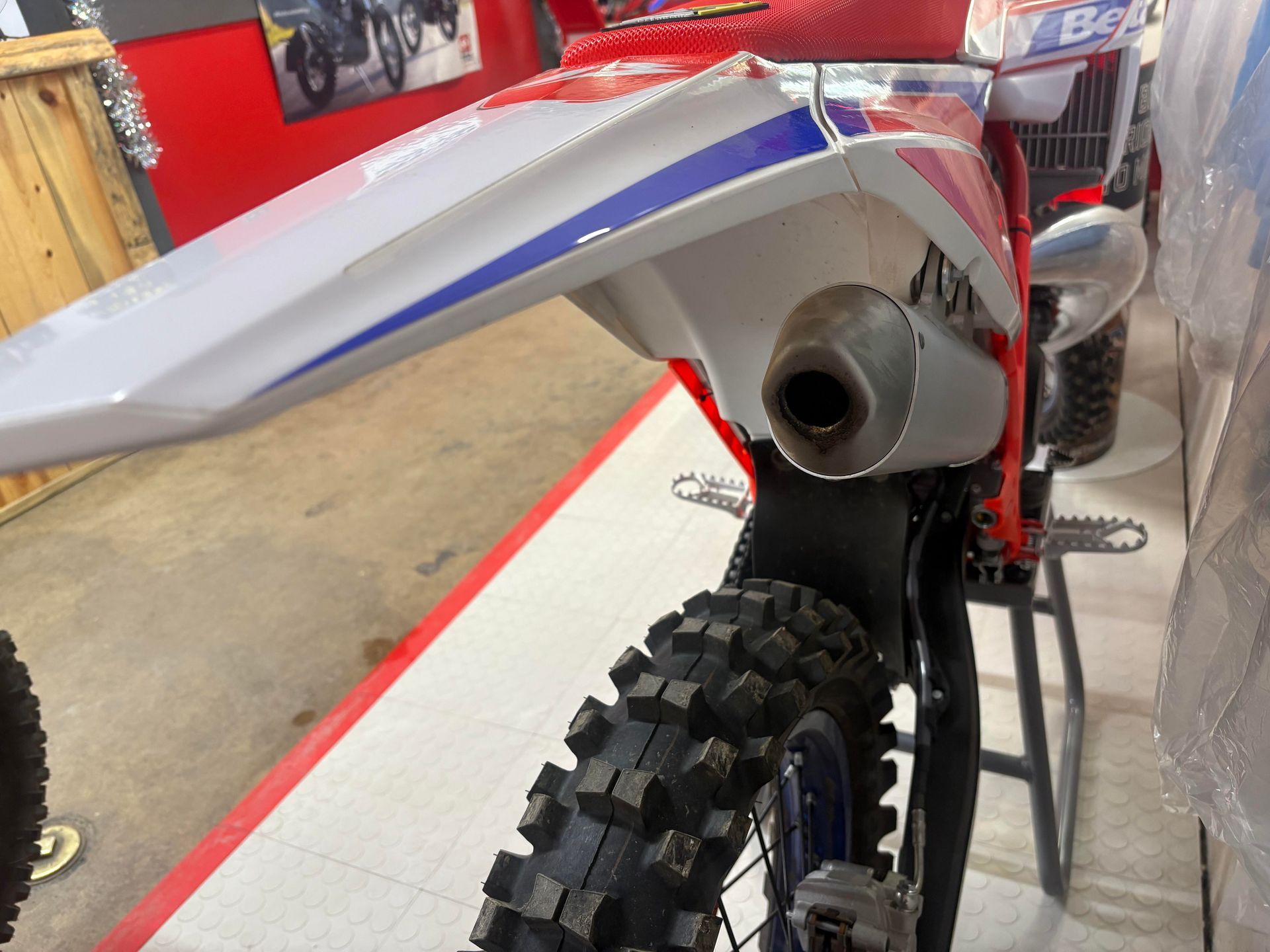 Rear view of a red dirt bike with a silver fender and exhaust in a workshop