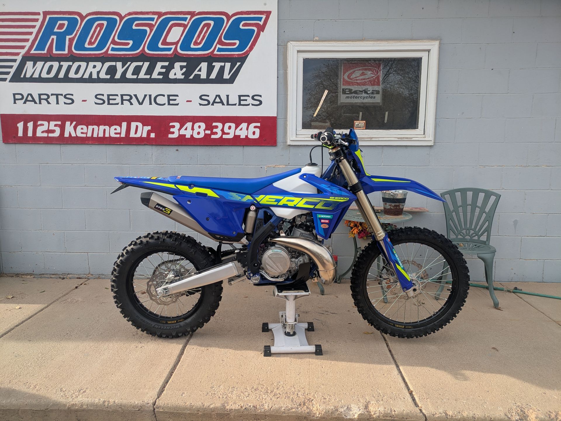Blue dirt bike on a stand outside Roscos Motorcycle ATV service shop.