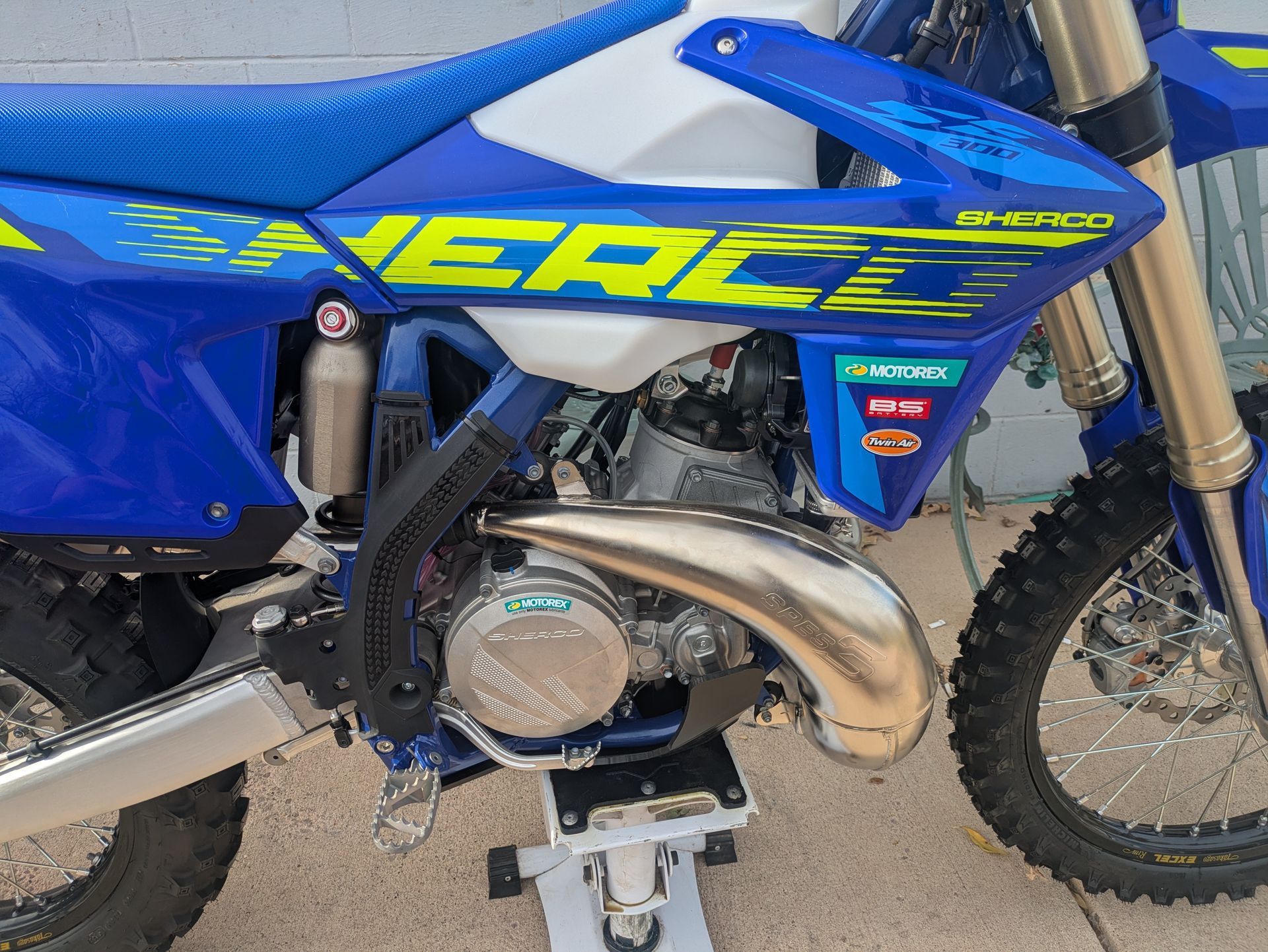 Close-up of a blue dirt bike with neon yellow graphics and a silver engine on a stand.
