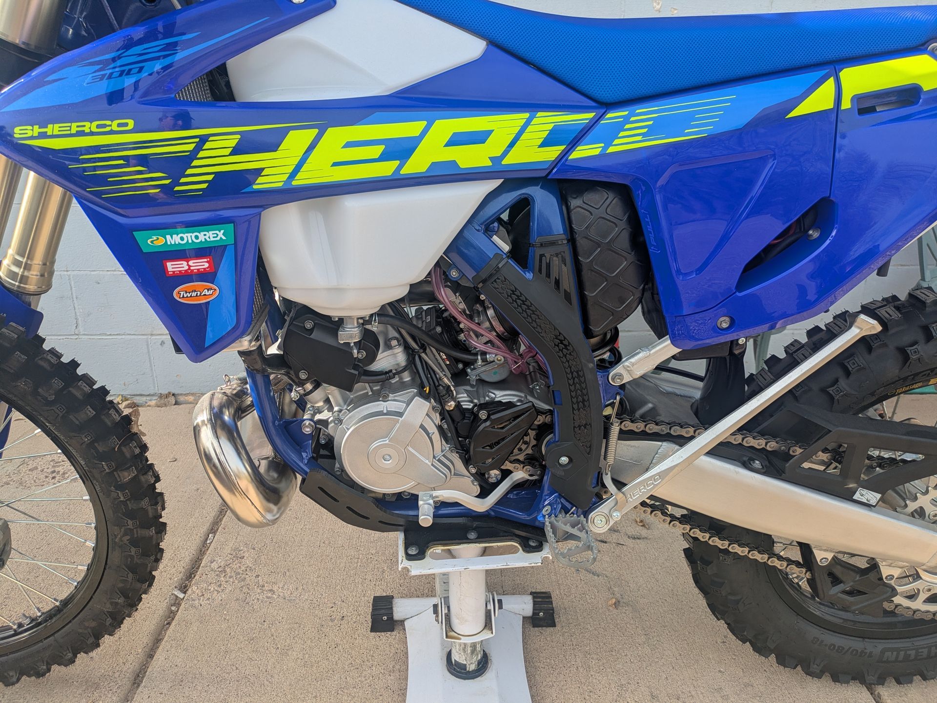 Blue dirt bike with “THERAPY” decal, showing engine and frame in a side view on a stand.