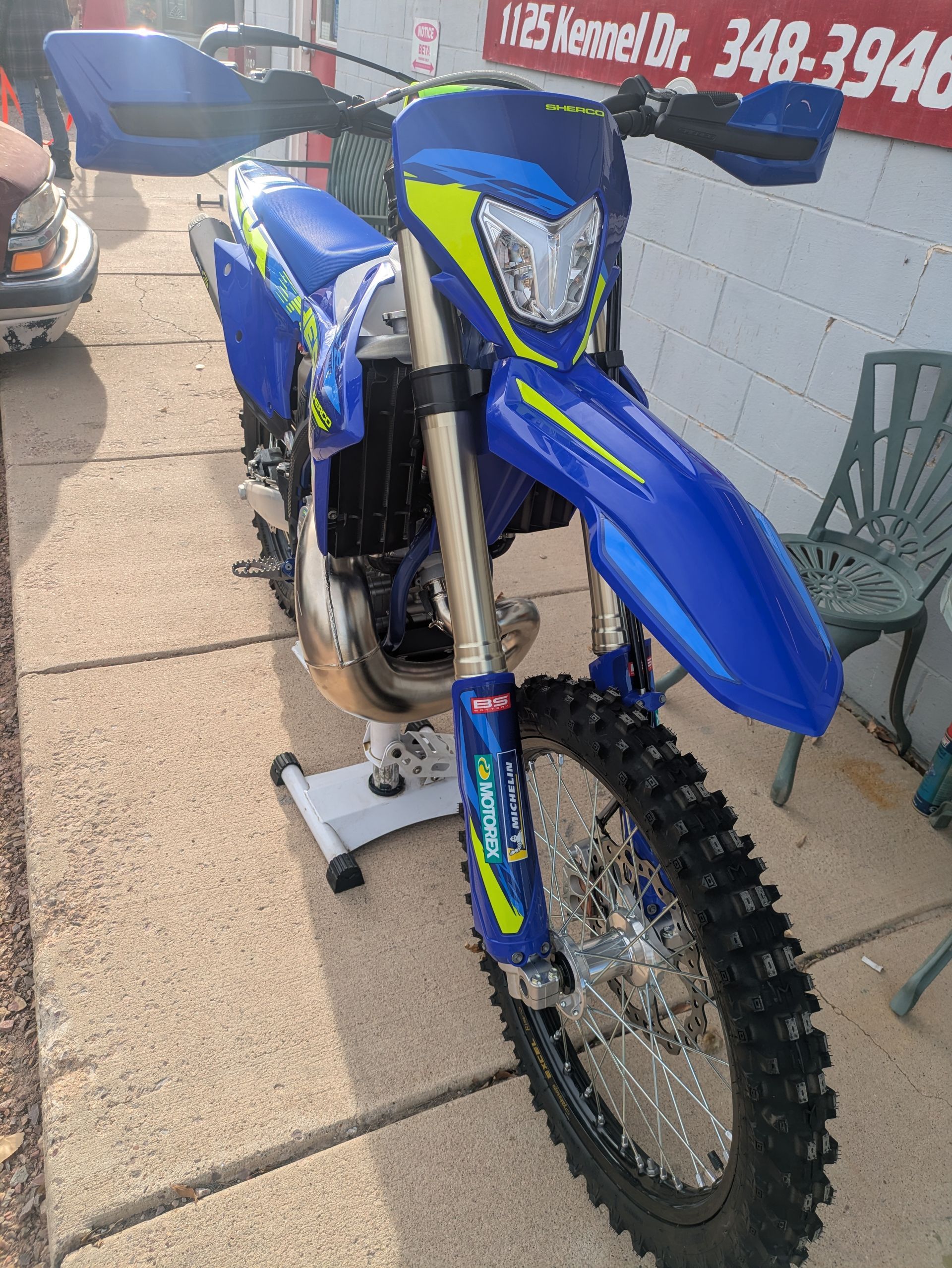 Blue dirt bike on a stand outdoors beside a wall.