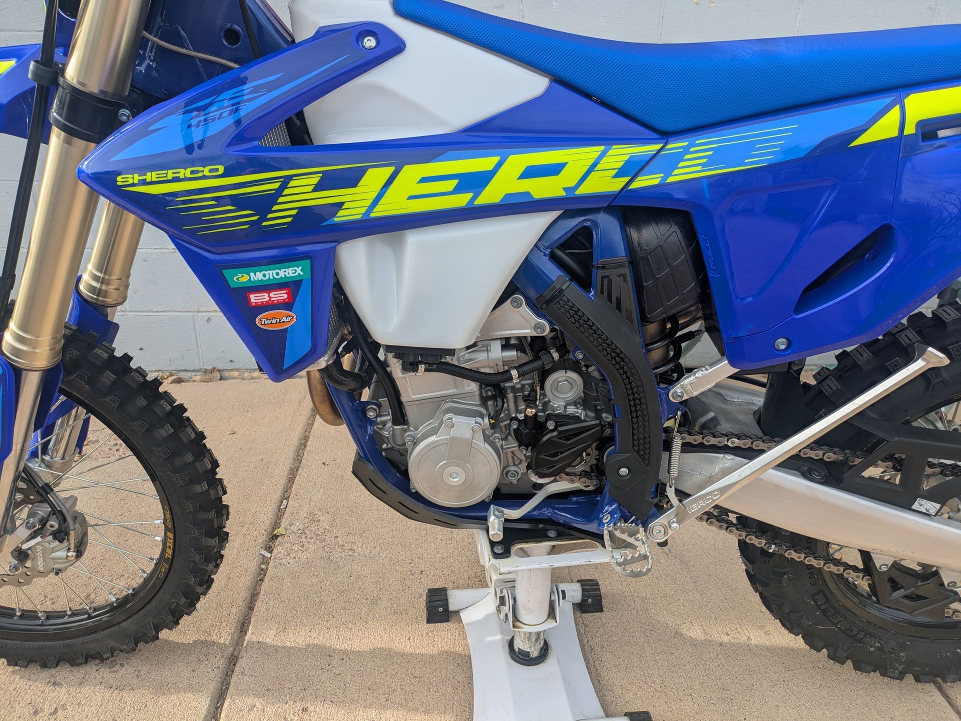 Blue dirt bike with yellow graphics parked on a stand on a concrete surface.