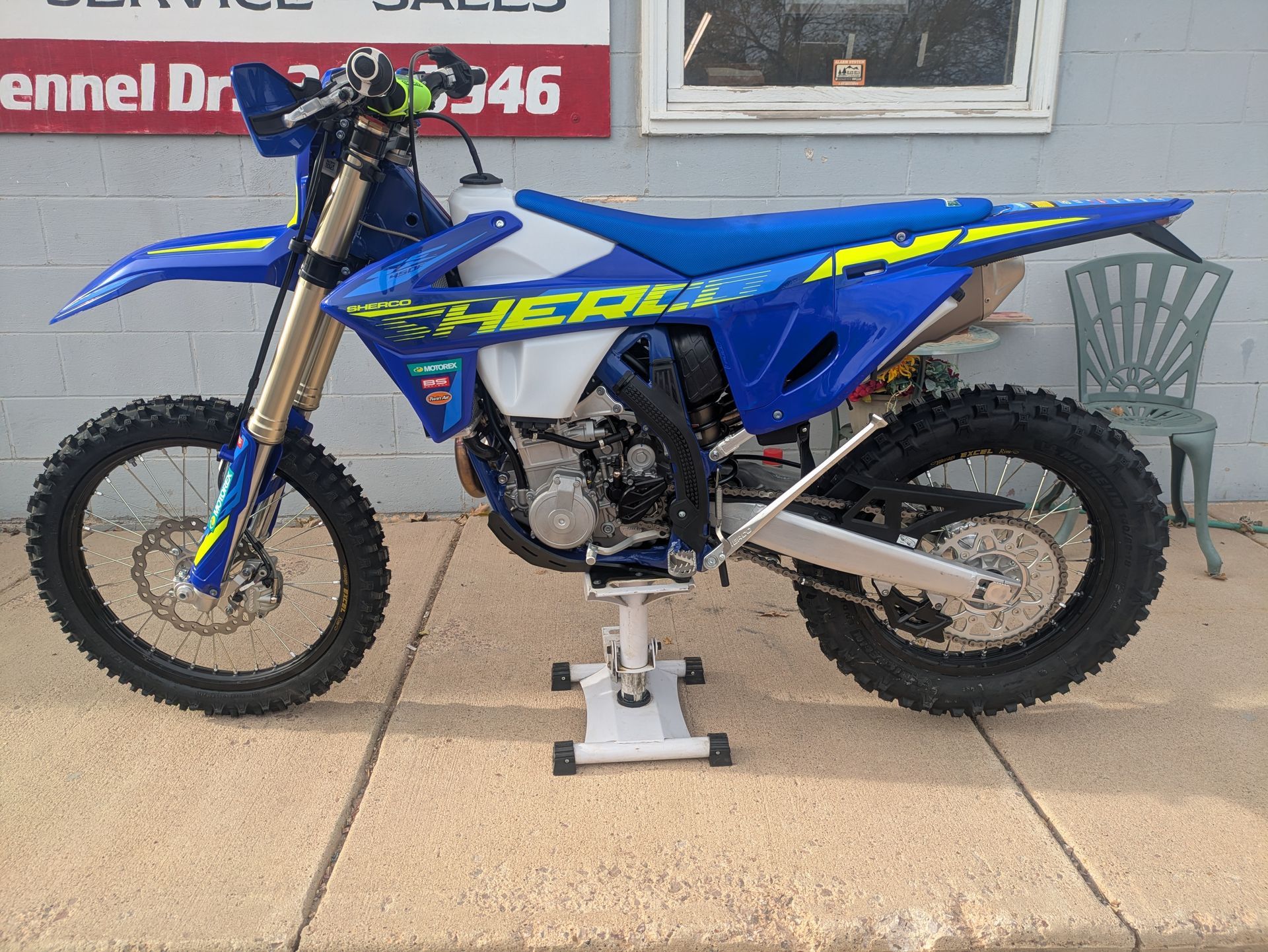 Blue dirt bike on a stand outdoors in front of a building entrance.