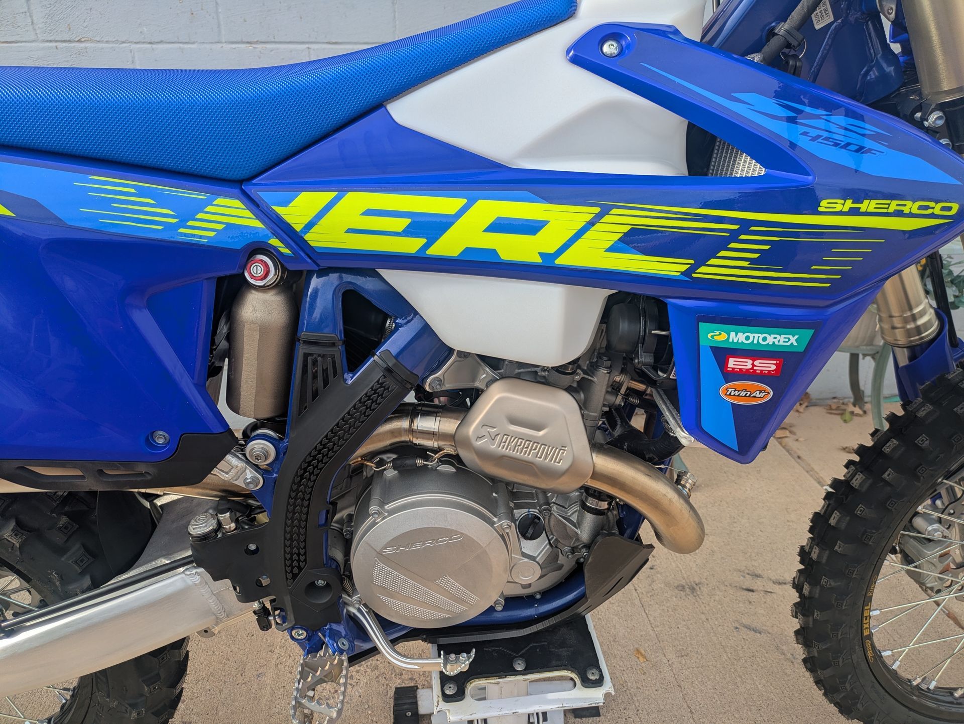 Blue dirt bike close-up with yellow graphics and visible engine under the seat