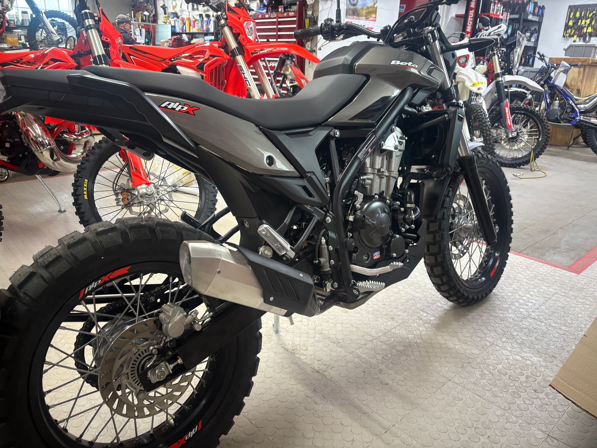 Black off-road motorcycle on display in a showroom, with red bikes in the background.