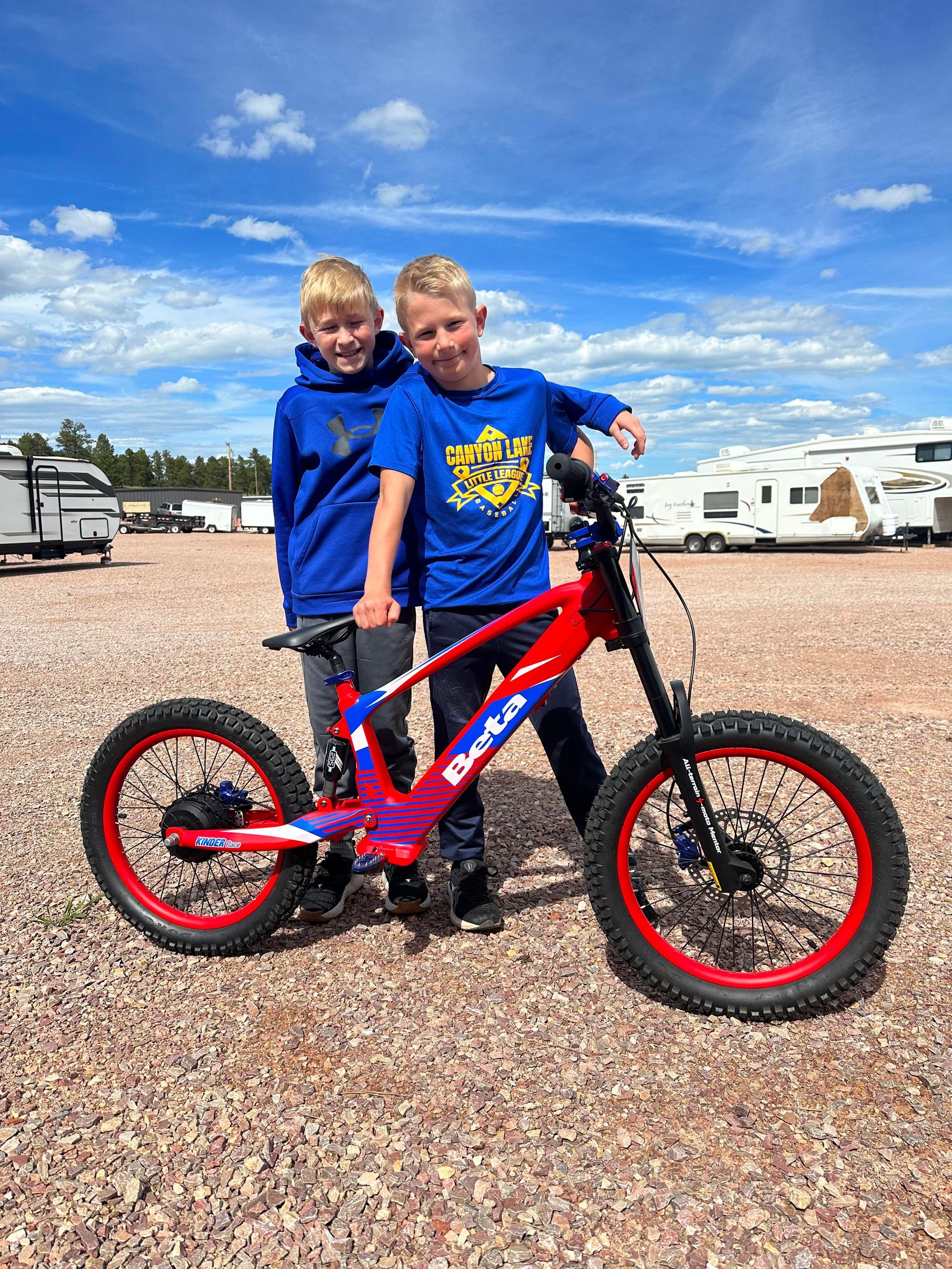 Two young boys are standing next to a red and blue bicycle.