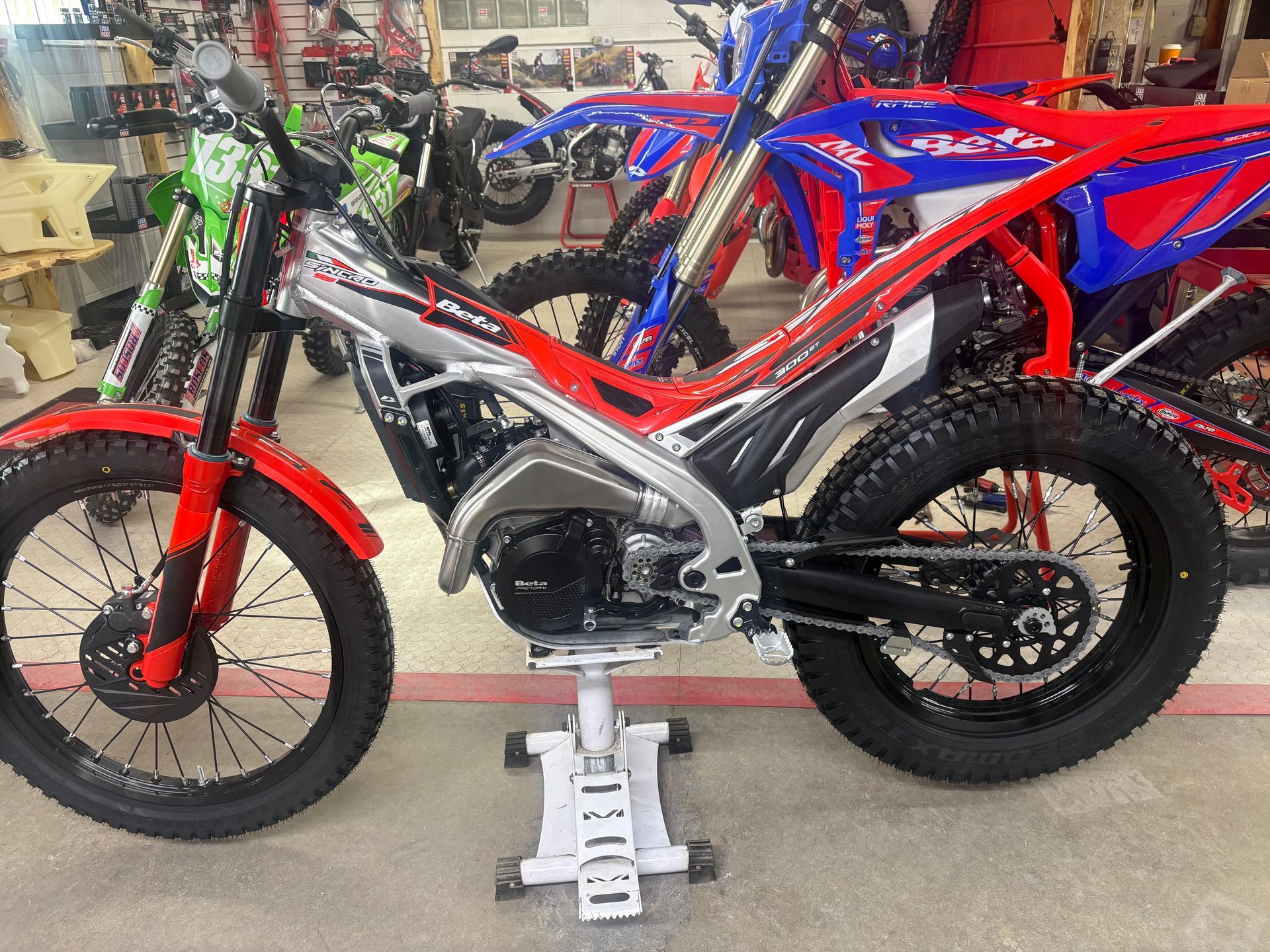 Red and black dirt bike on display in a shop, with other motorcycles in the background.