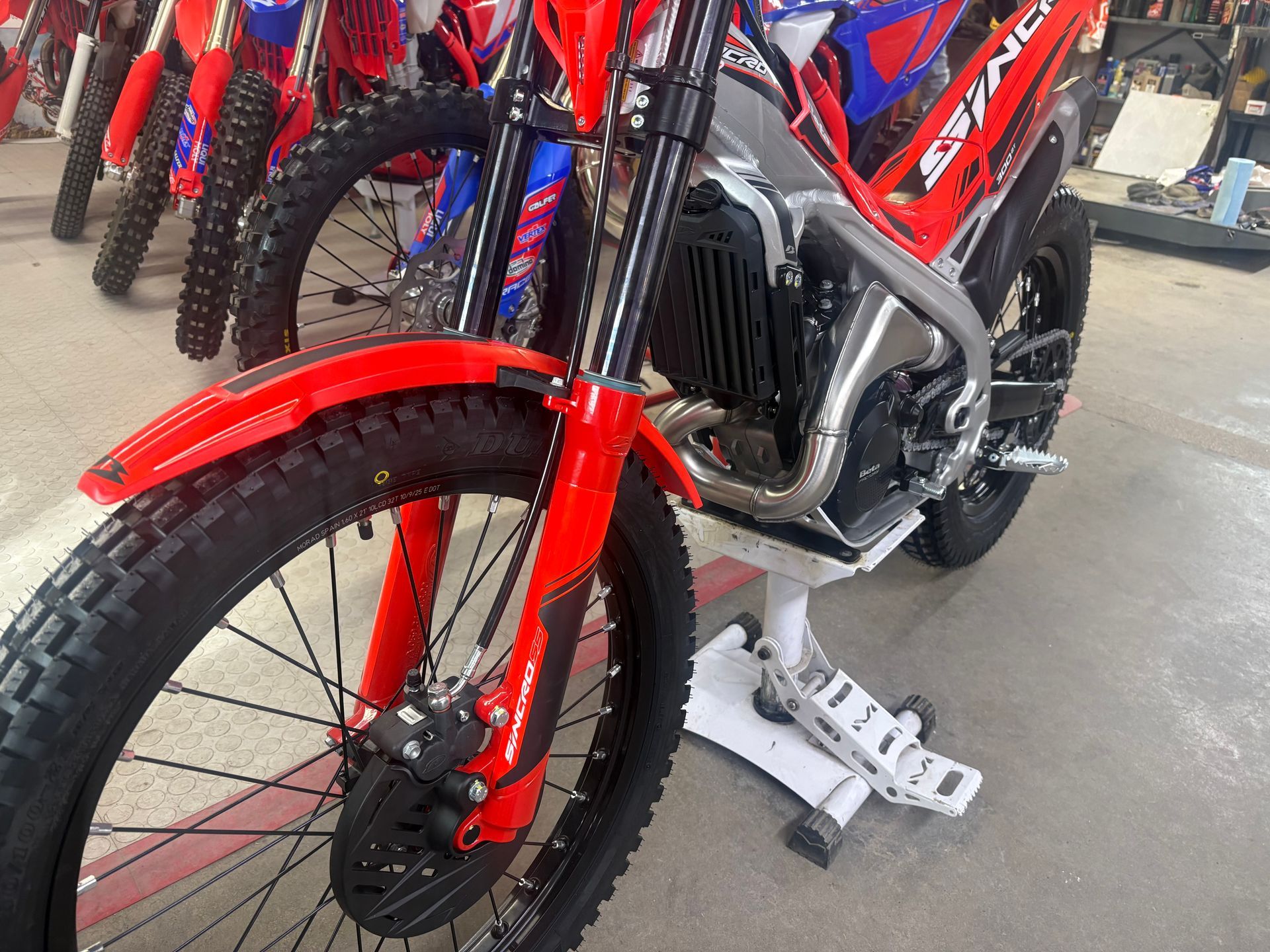Red dirt bike with front wheel and fork in a showroom, with other bikes in the background.