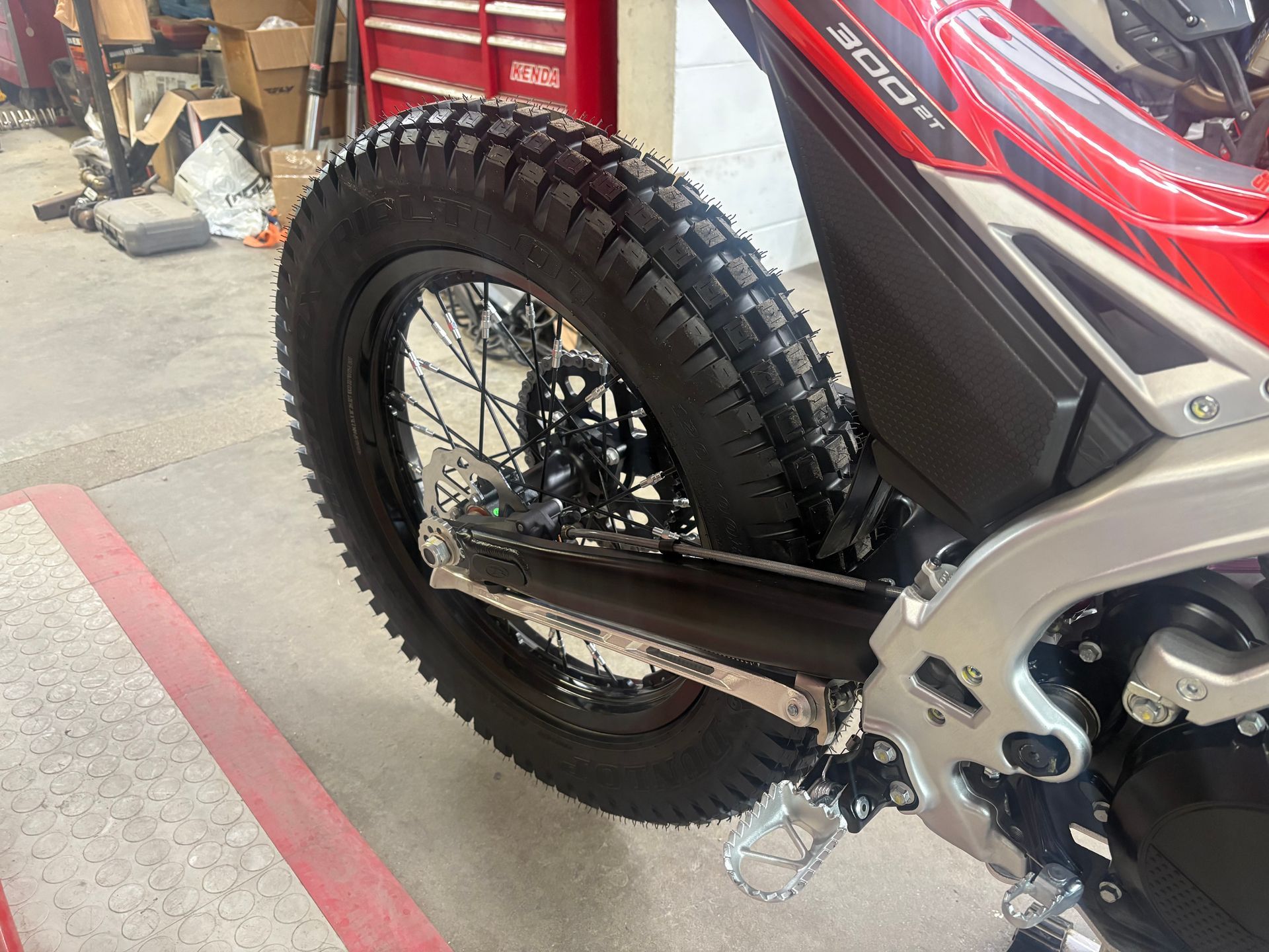 Rear wheel and footpeg of a black off-road motorcycle in a garage with red tool cabinets