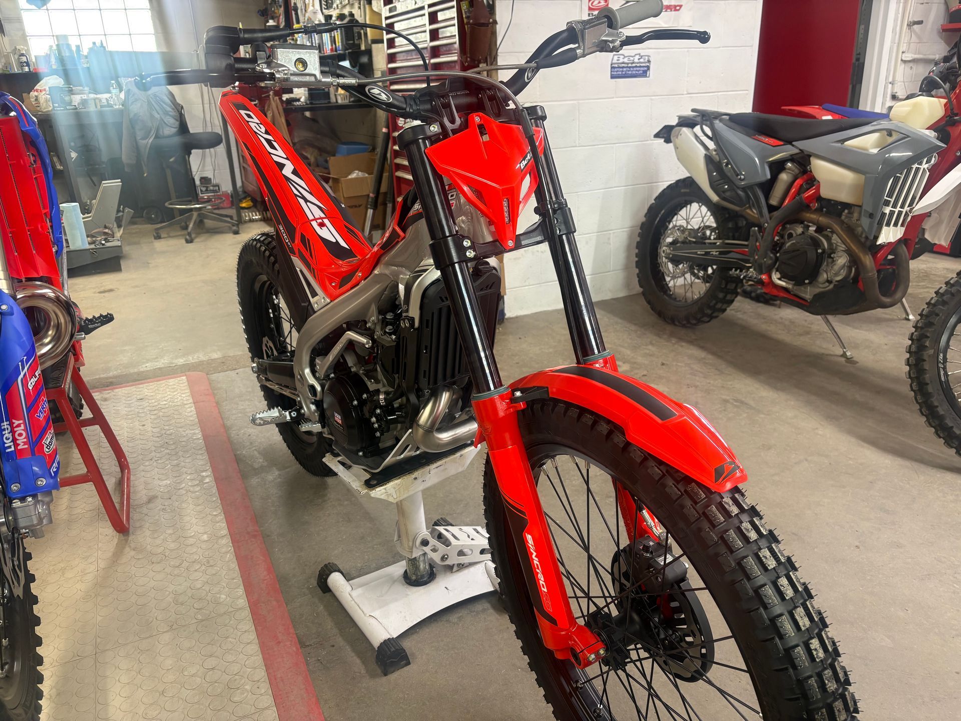 Red off-road motorcycle on a stand in a showroom, with other dirt bikes in the background.