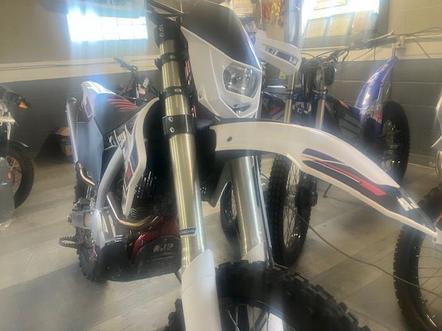 A dirt bike is parked in a garage next to other dirt bikes.