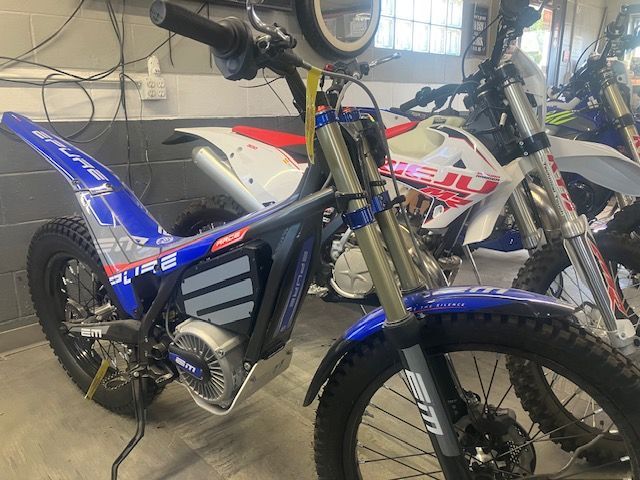 A blue dirt bike is parked next to a white dirt bike in a garage.