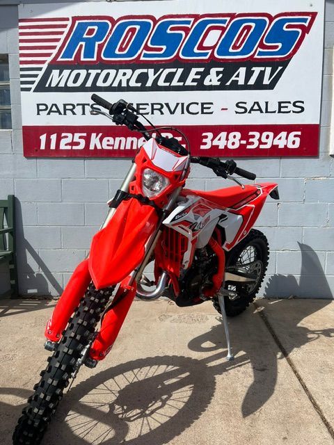 Red dirt bike parked in front of Rosco’s Motorcycle & ATV service and sales shop sign.