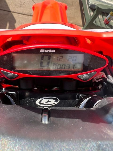 Close-up of a red snowmobile dashboard with a digital display and handlebars visible.
