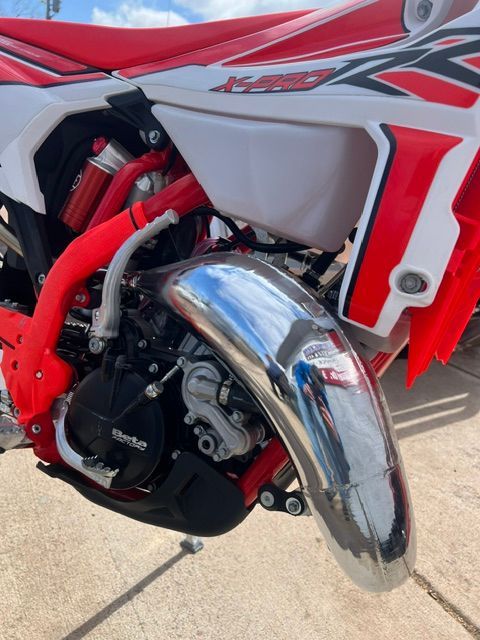 Close-up of a red and white dirt bike engine with a chrome exhaust on concrete.