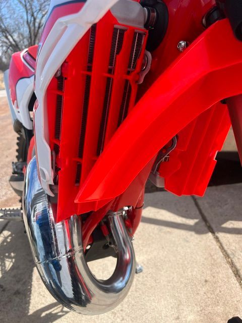Close-up of a red motocross bike's engine and chrome exhaust pipe on pavement