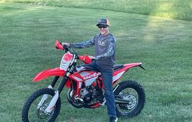A man is standing next to a dirt bike in a grassy field.