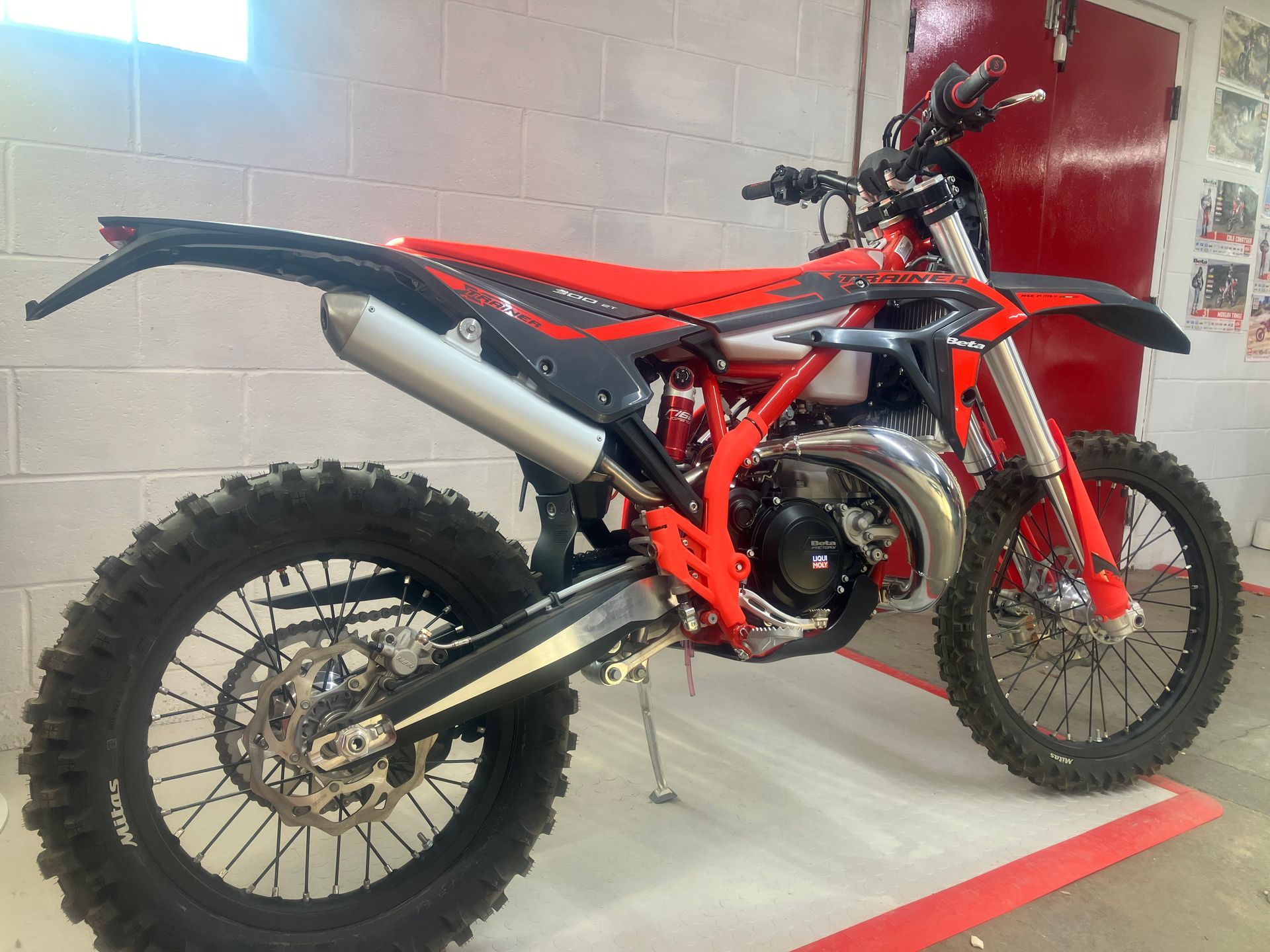 A red and black dirt bike is parked in front of a brick wall.