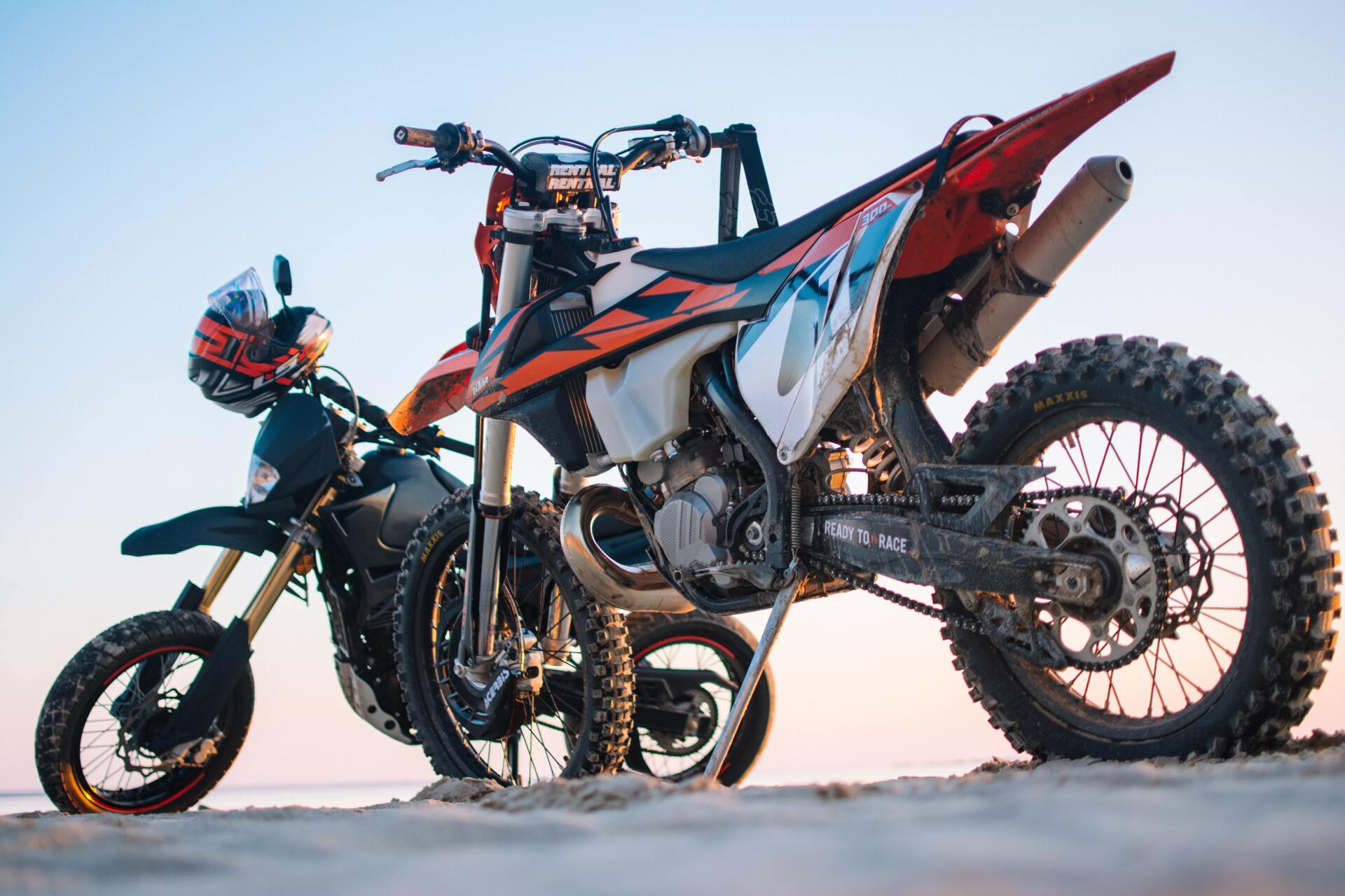 Two dirt bikes are parked next to each other on the beach.