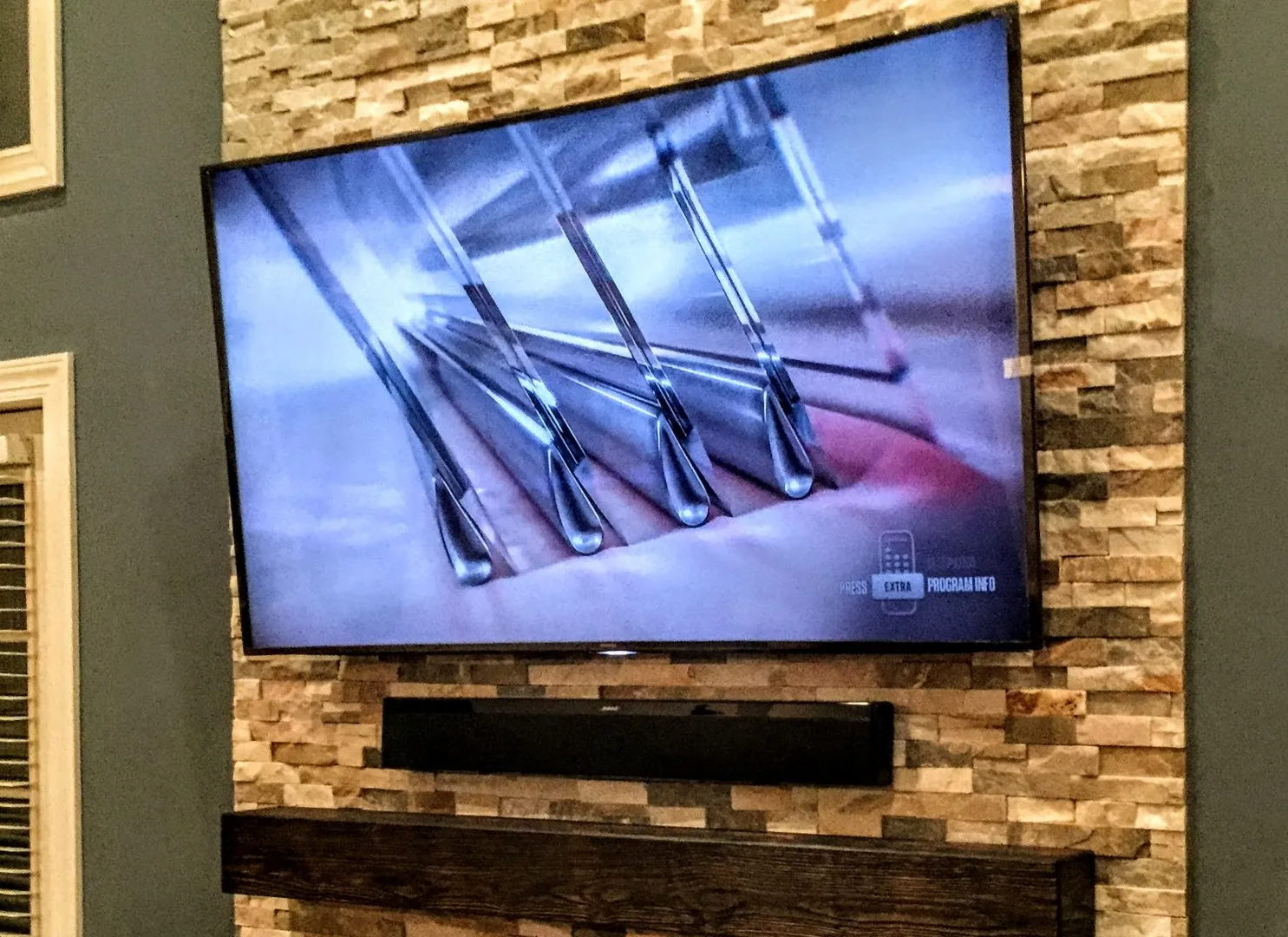A large curved TV mounted on a stone accent wall, with a soundbar below it.