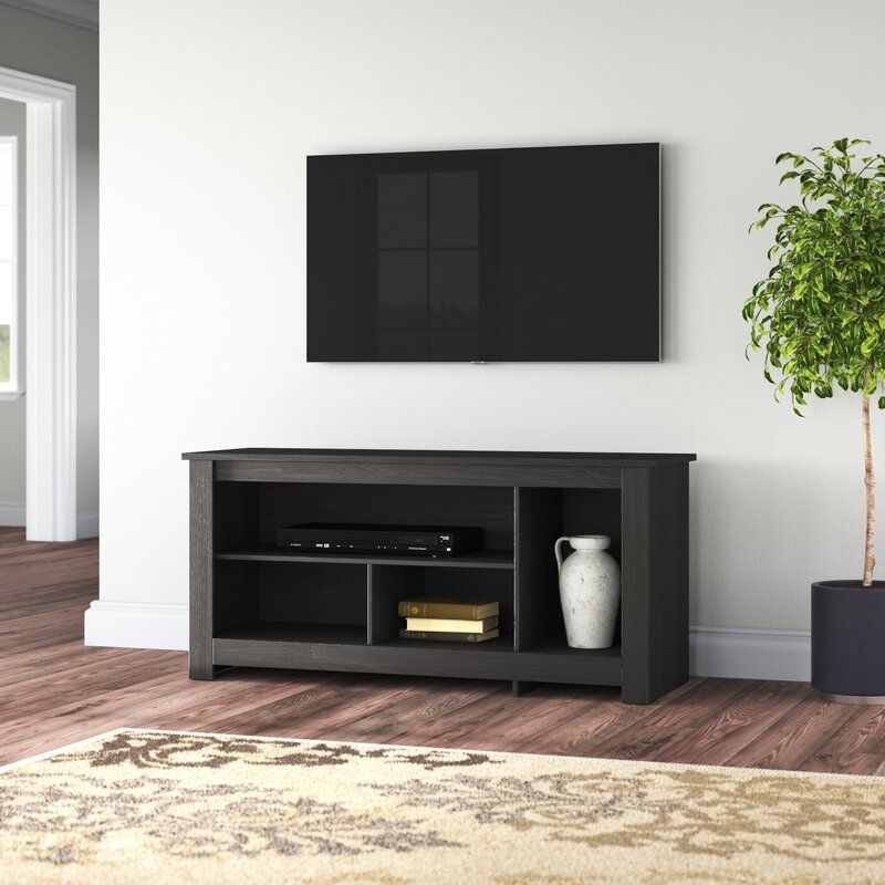 Dark gray TV stand with entertainment system, beneath a mounted TV, against a white wall; tree and rug in room.