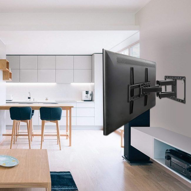 A black TV mounted on a swivel arm in a modern living room, with a kitchen visible in the background.