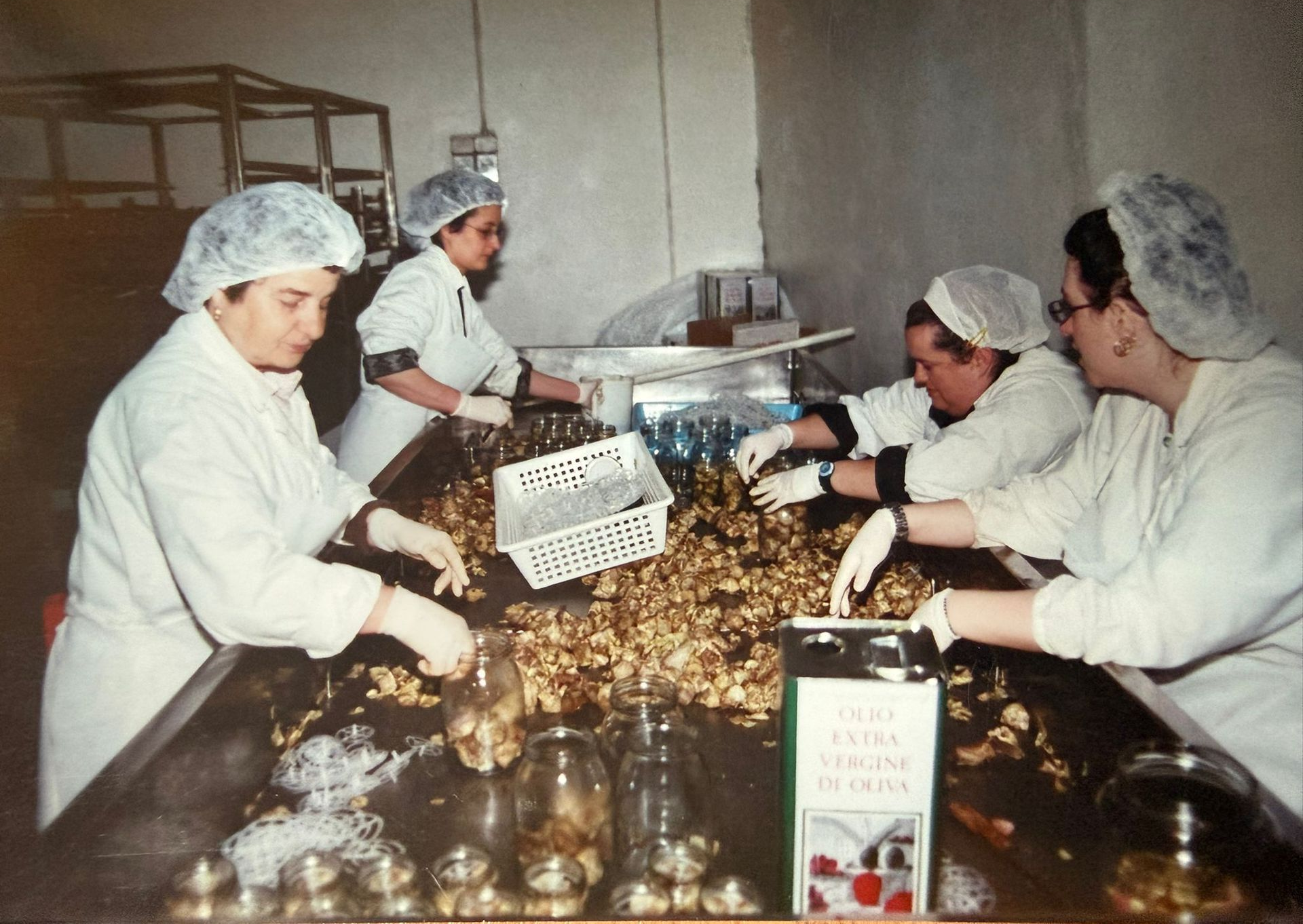 Operai in uniforme bianca e con retine per capelli selezionano piccoli prodotti marroni su un nastro trasportatore in una fabbrica.