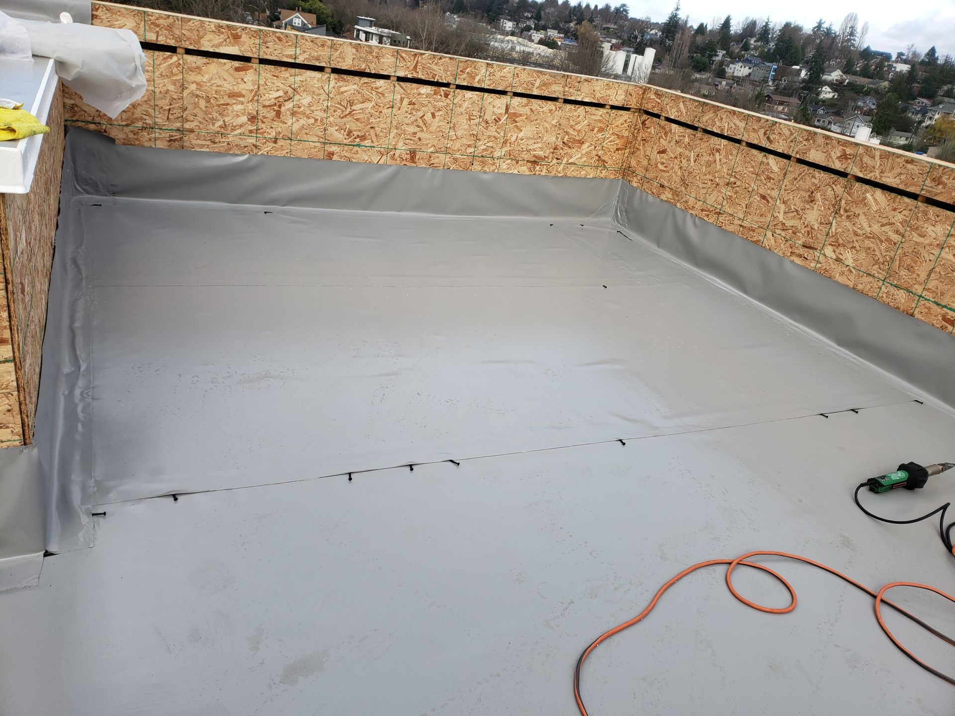 Gray rooftop deck with plywood walls and an orange cord on the floor