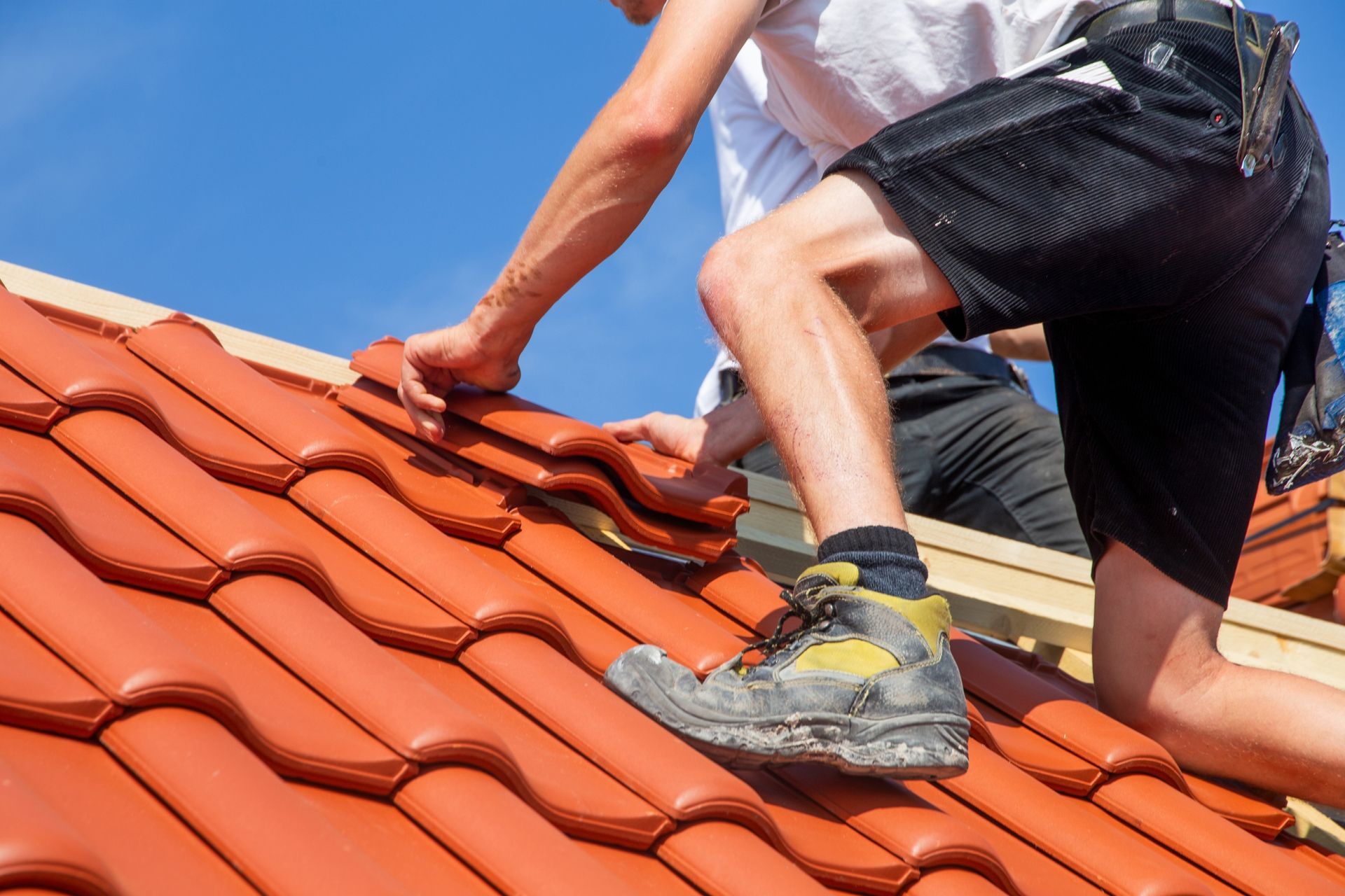 Worker installing red roof tiles on a rooftop under a blue sky