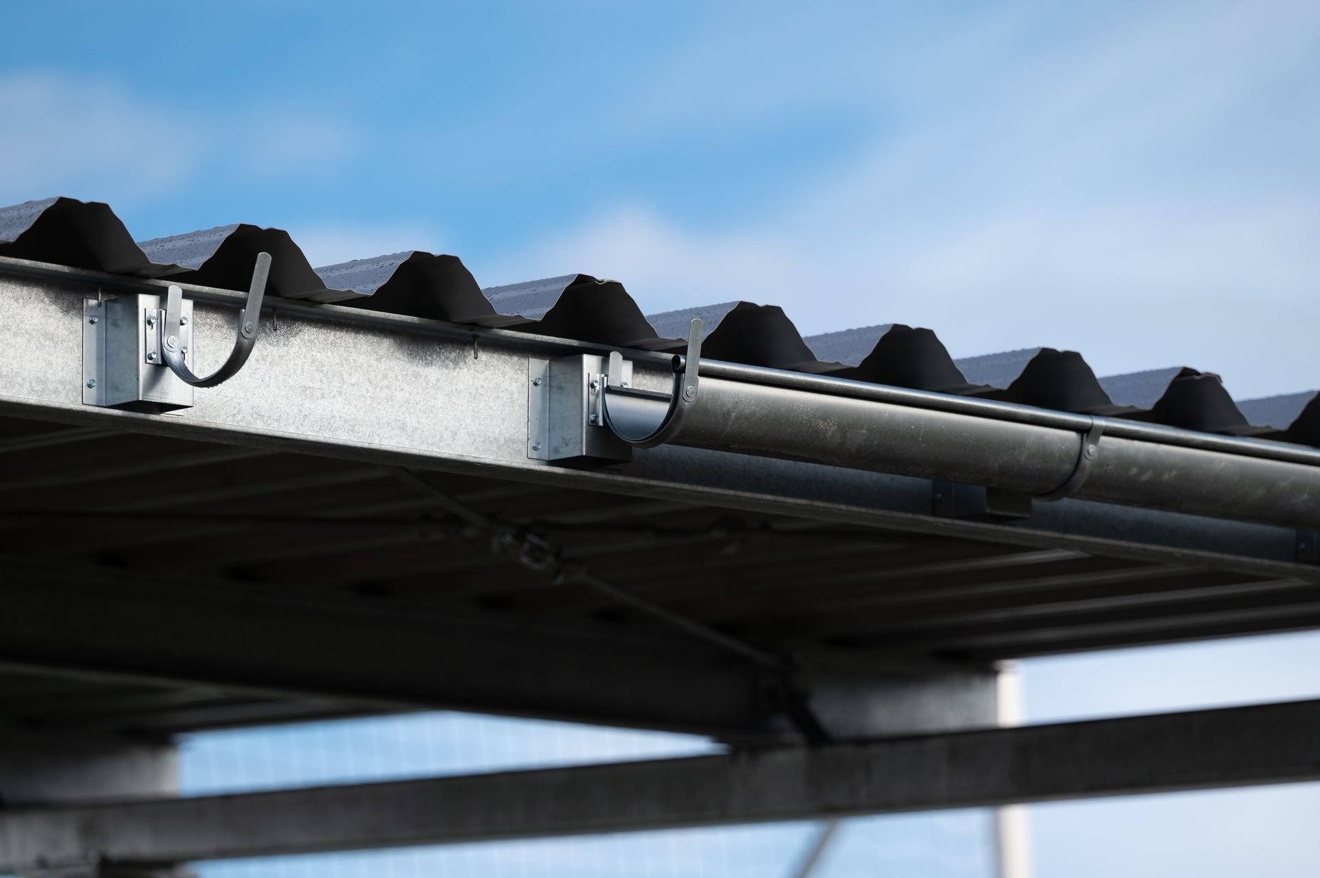 Close-up of a corrugated metal roof edge with gutters against a blue sky