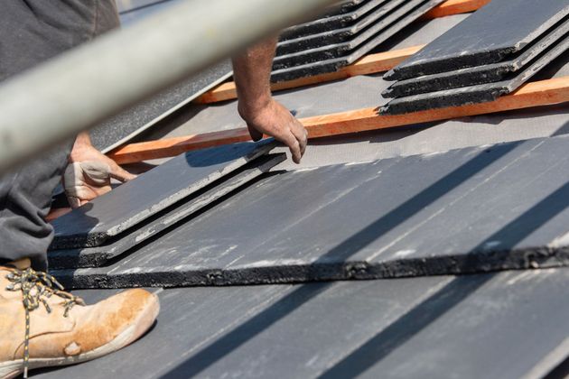 Workers installing dark roof panels on a sloped rooftop with a ladder in the foreground