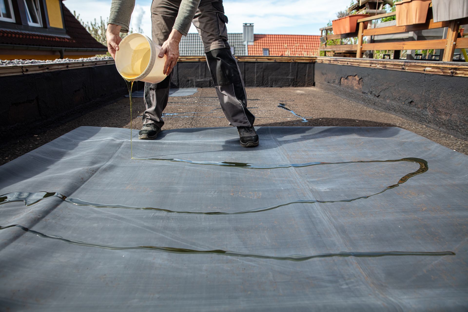 Person applying black roofing material with a brush on a flat rooftop