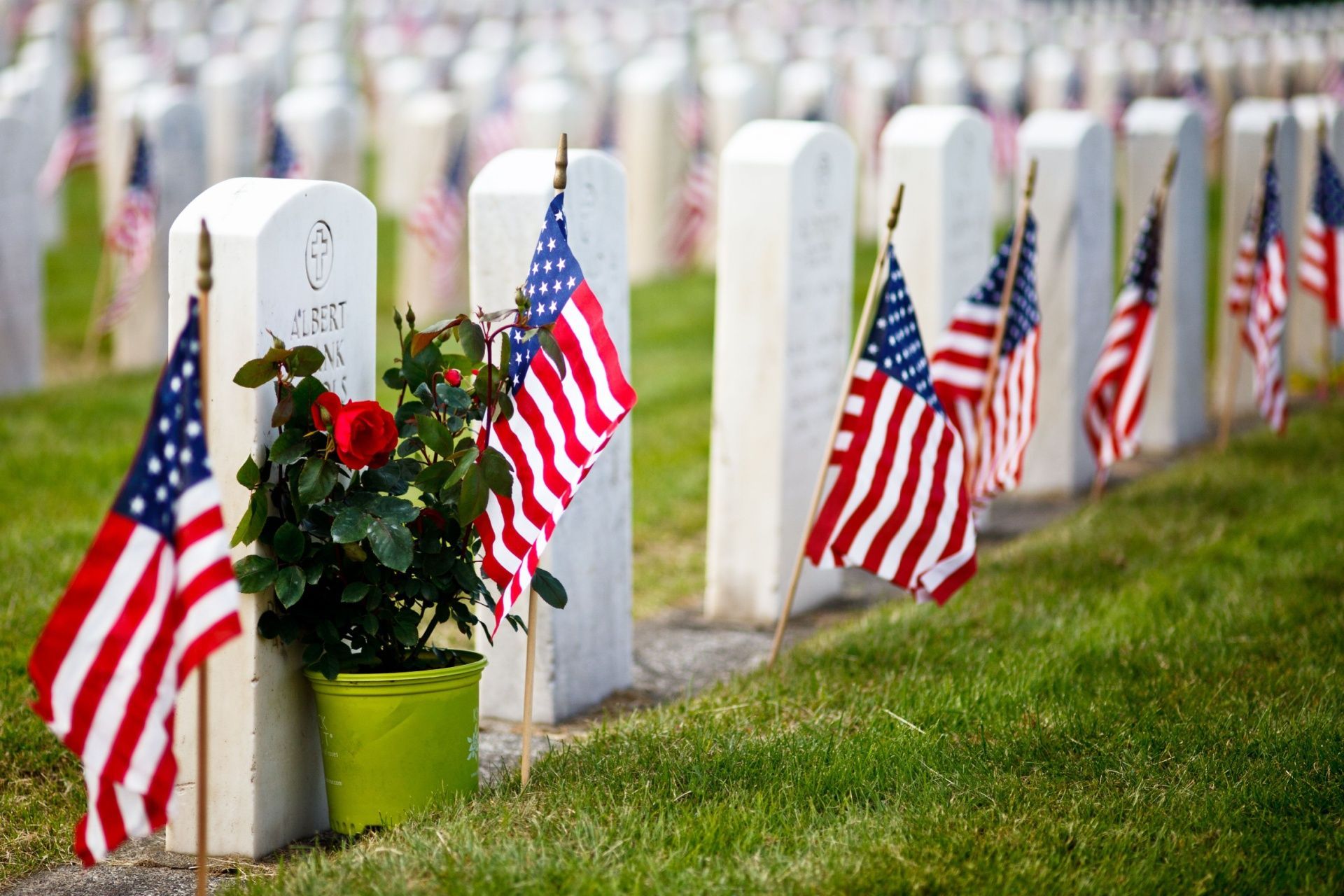 Rows of white gravestones with American flags and red flowers at a memorial cemetery