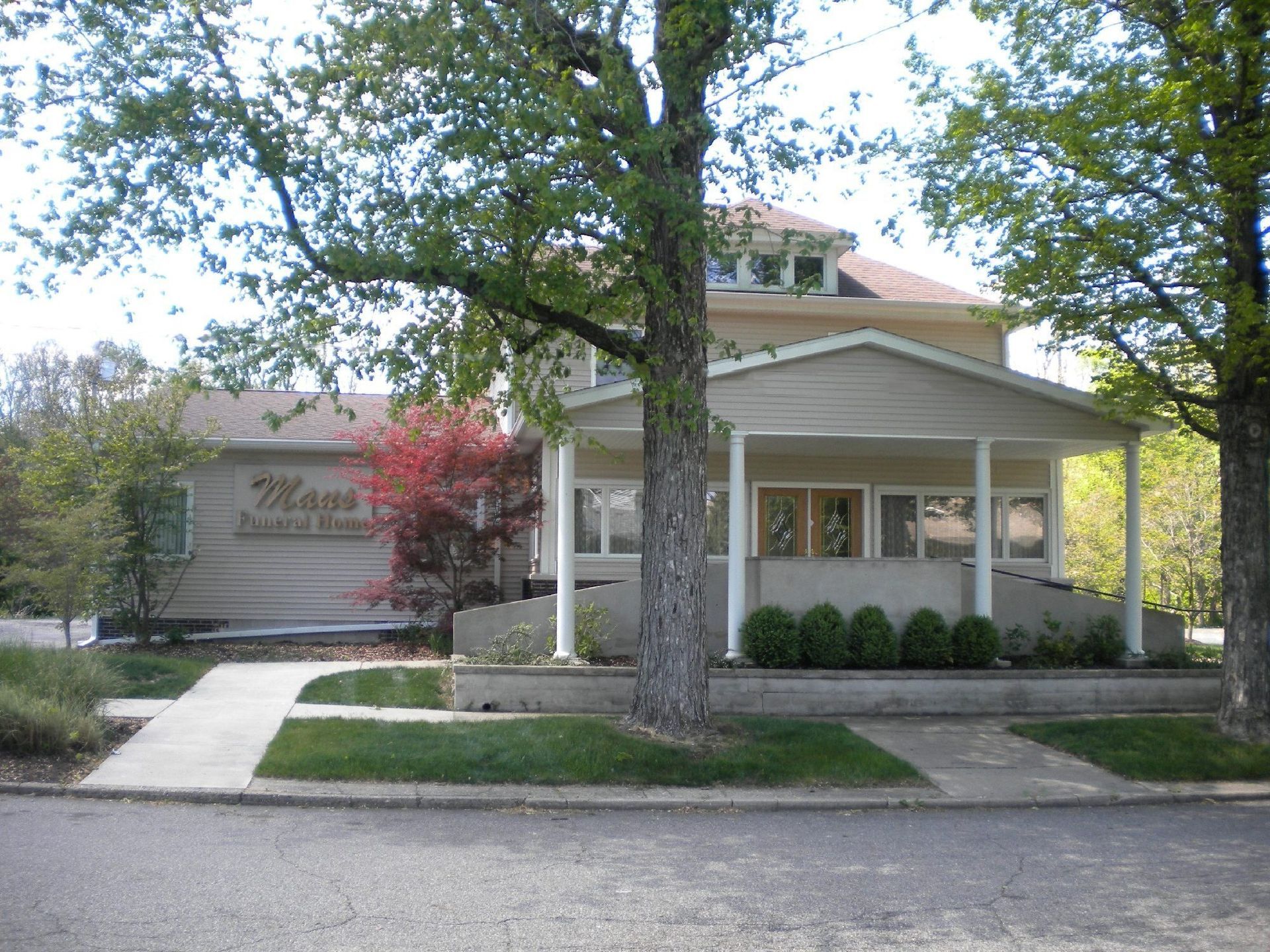 Single-story beige building with a front porch, trees, and a sidewalk in the foreground
